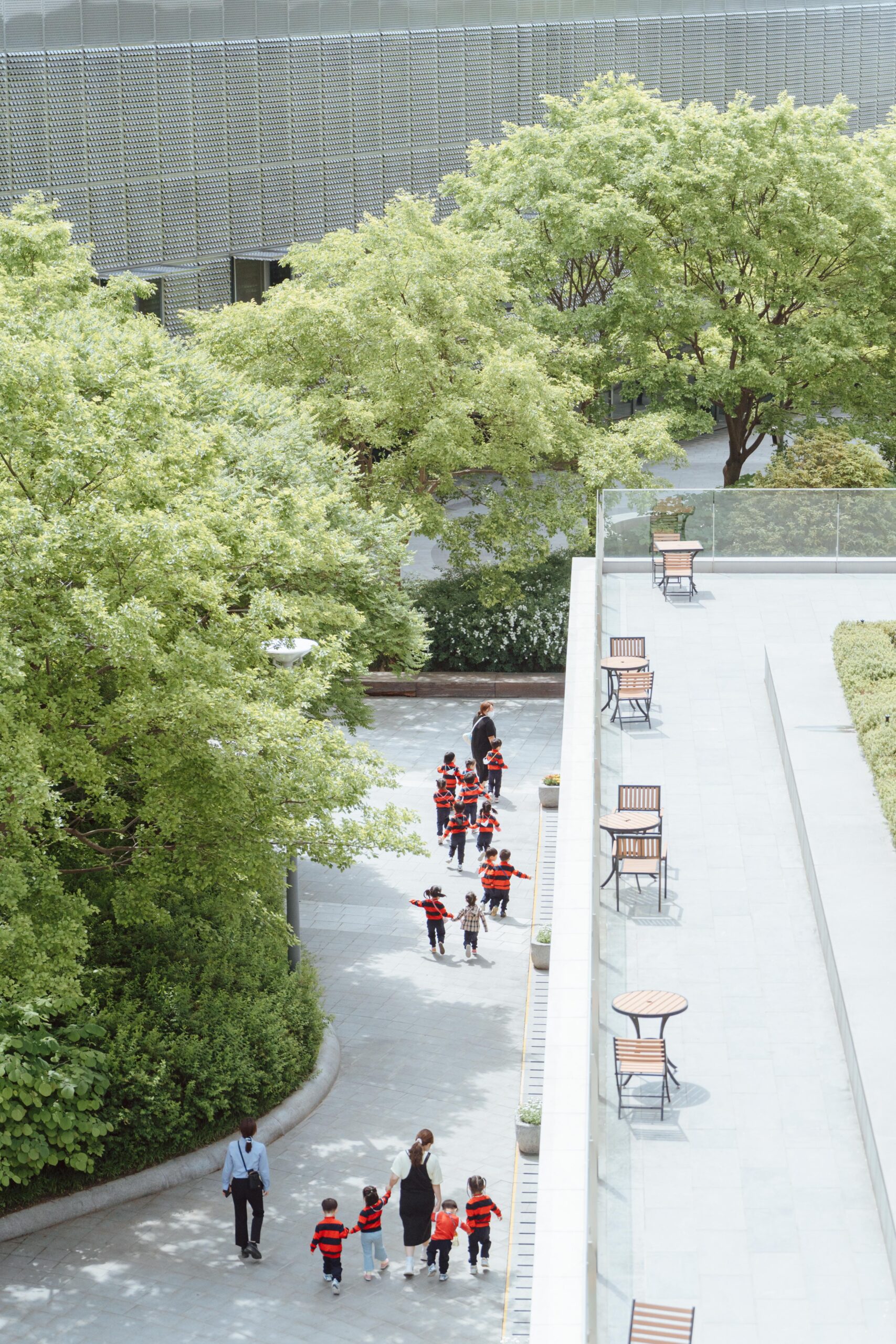 Students on a school trip through a park with a raised area with seating. Teachers accompany them, guiding the way.