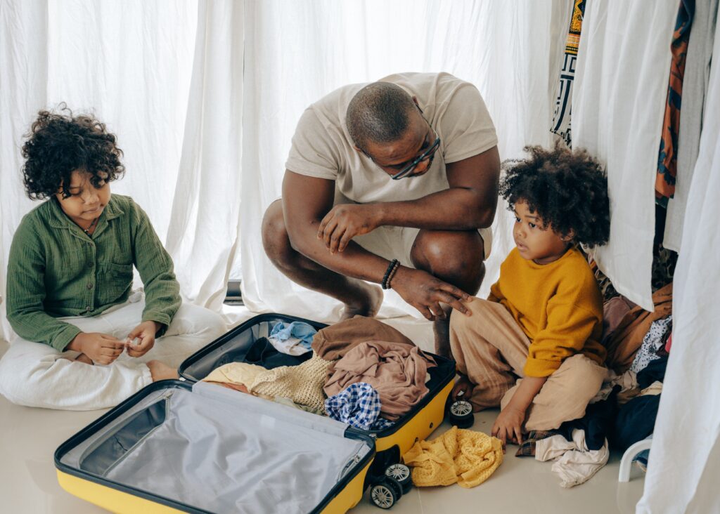 Children packing to go on a school trip. The suitcase is open on the floor and the father is discussing with the child.